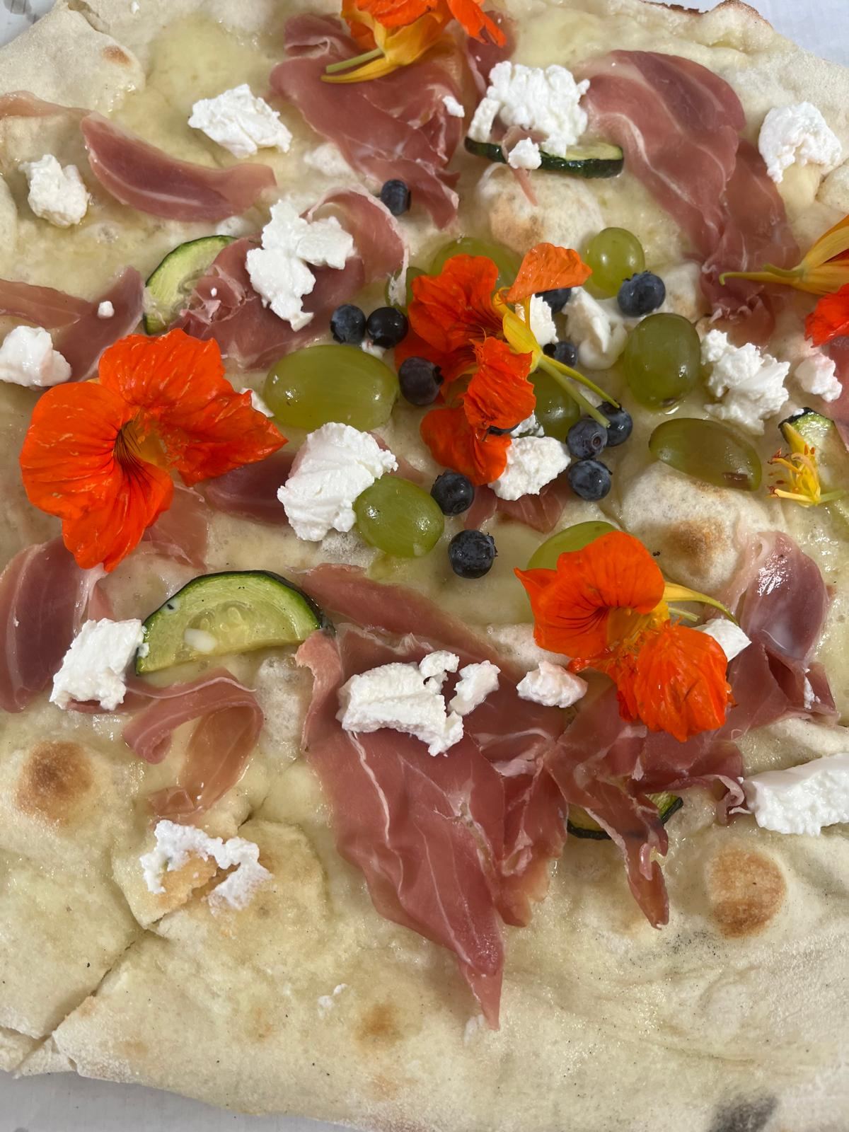 Pizza z prosciutto, kwiatami jadalnymi i winogronami
