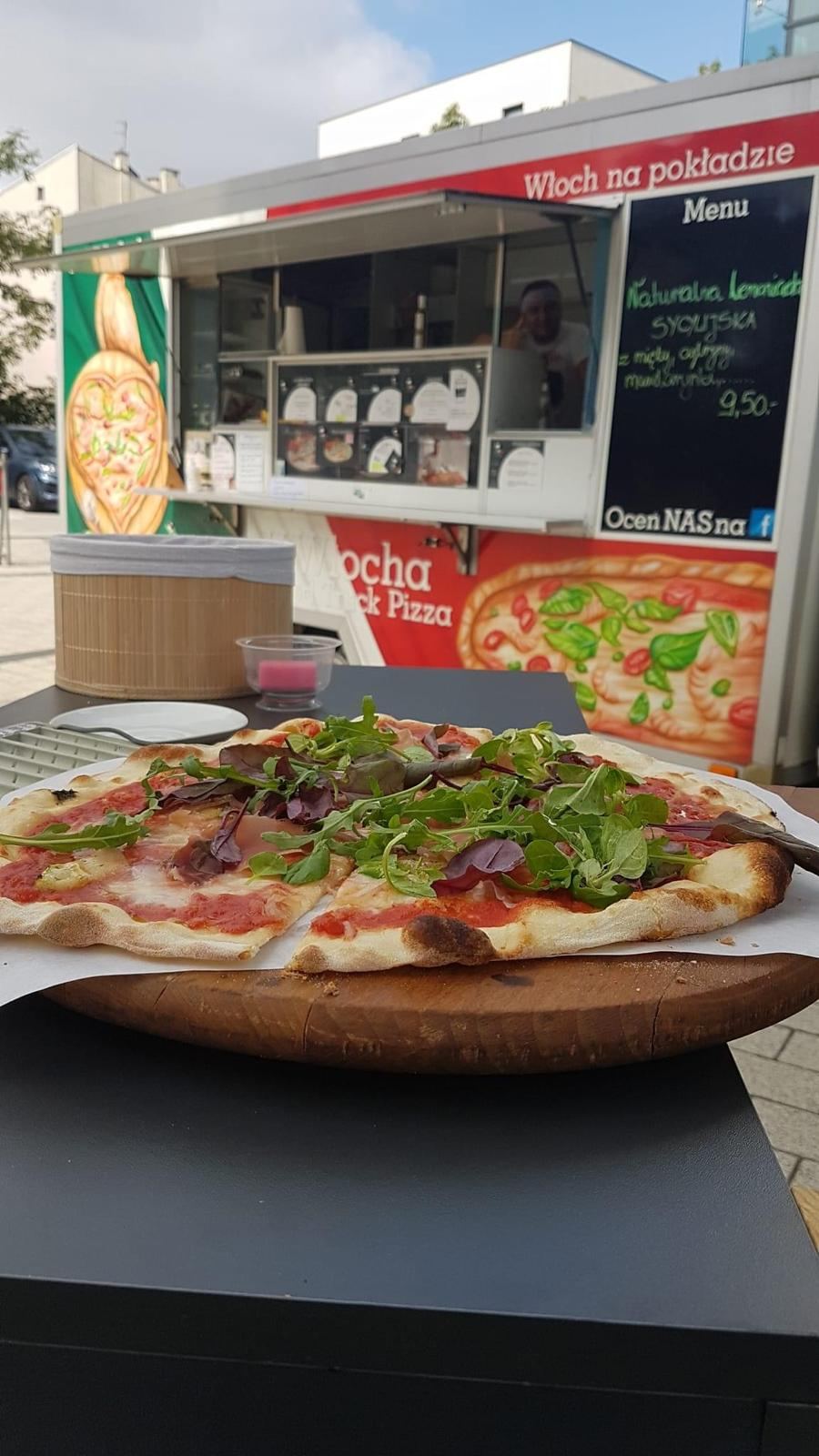 Pizza z rukolą na drewnianej desce przed food truckiem